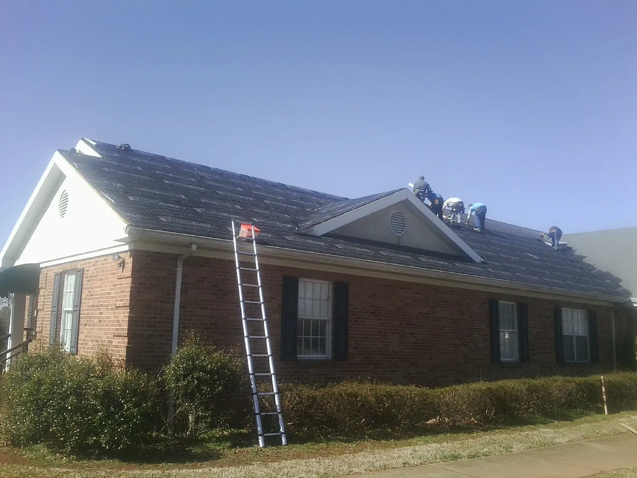 Crew tearing shingles off a brick ranch roof with a ladder set — Emergency Roof Repair work by our crew in Prairie Du Sac