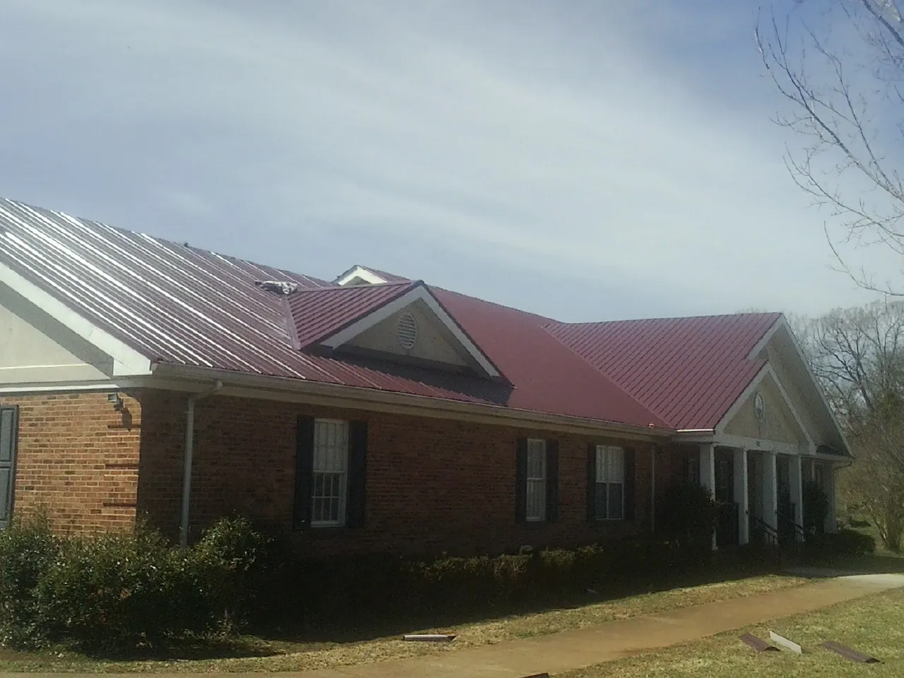 Red metal roof with gabled entries on a long brick building, from a Hail Damage Roof Repair job in Prairie Du Sac