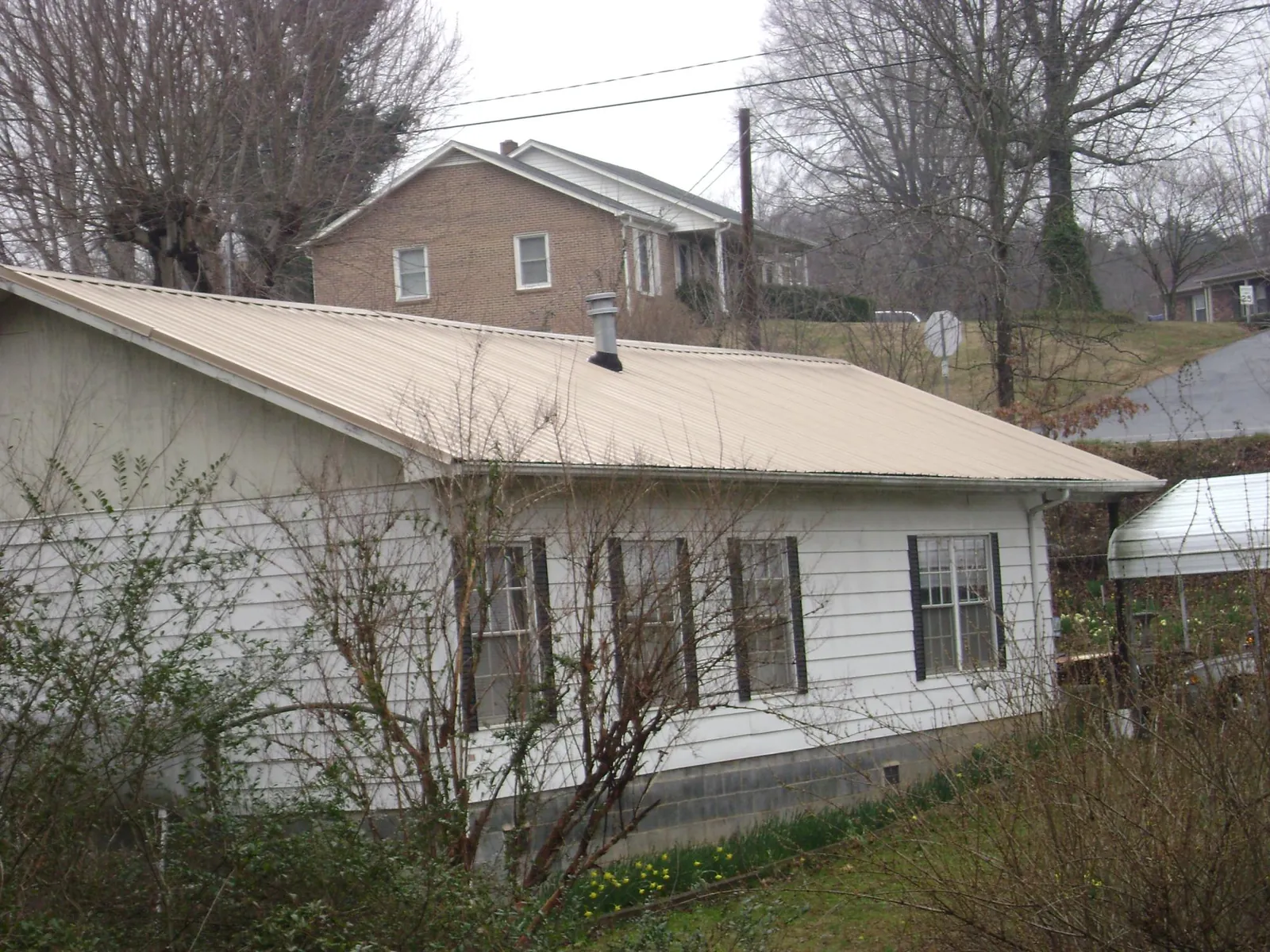 Tan metal roof on a white sided house set into a hillside — Commercial Roofing by Roofing Brothers in Prairie Du Sac